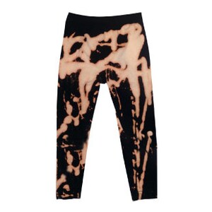 May include: Black leggings with a bleach-splattered design. The bleach creates a unique pattern of white and light gray on the black fabric.