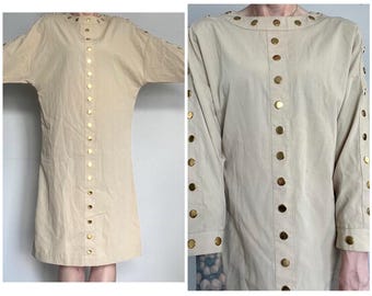 May include: A beige long-sleeved tunic dress with gold buttons down the front and on the sleeves.