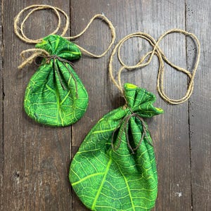 May include: Two green leaf-patterned drawstring bags with brown twine ties. The bags are hanging from the twine.