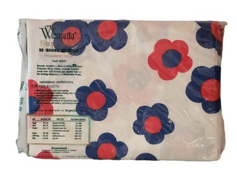 Puede incluir: Una sábana plana blanca con un estampado floral rojo y azul. La sábana está empaquetada en plástico y tiene una etiqueta que dice "Vamsutta Super No Ironing Necessary Permanent Press Flat Sheet".