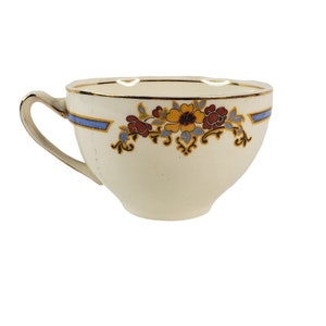 May include: A white teacup with a blue and gold floral design. The cup has a gold rim and a handle.