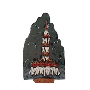 May include: A ceramic wall sculpture depicting a human pyramid, or "castell", with a person at the top. The sculpture is painted in red, white, and black, and is set against a dark gray background.