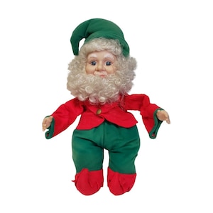 May include: A plush toy elf with a green hat, red jacket, and green pants. The elf has a white beard and a smiling face.