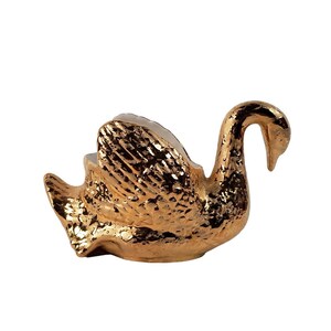 May include: A gold swan-shaped planter with a textured surface. The planter is made of ceramic and has a white interior.