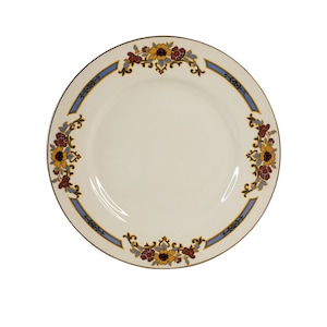 Könnte beinhalten: Cremefarbene Keramikplatte mit floralem Design. Der Teller hat einen braunen Rand und einen dekorativen Rand mit blauen, gelben und kastanienbraunen Blumenmustern. Das Design ist symmetrisch, mit den floralen Elementen um den Tellerrand angeordnet.