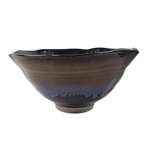 May include: A ceramic bowl with a unique, organic shape. The bowl features a gradient of colors, transitioning from a dark brown to a deep blue hue. The rim has a wavy design, and the base is a light gray color.