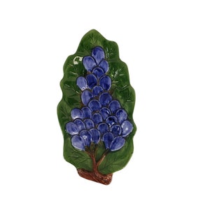 May include: A ceramic grape dish with a green leaf design and a cluster of blue grapes. The dish is perfect for serving snacks or appetizers.