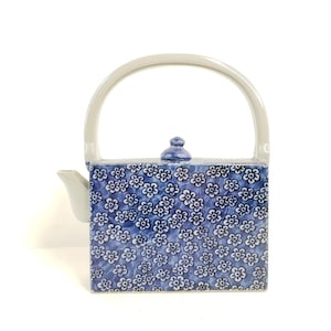 May include: A blue and white ceramic teapot with a floral pattern. The teapot has a square body and a white handle.