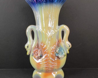 May include: A ceramic vase with a blue, yellow and orange iridescent glaze. The vase is shaped like two swans with their necks intertwined. The swans have detailed faces and there are roses on their necks.