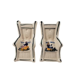 May include: A pair of white ceramic salt and pepper shakers shaped like chairs with green trim and painted figures.