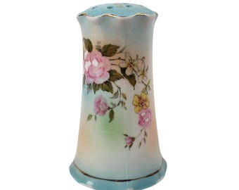 May include: A vintage porcelain salt shaker. It has a light blue top and base, and a floral design of pink, yellow, and white flowers with green leaves. The shaker is cylindrical with a flared base and a scalloped top.