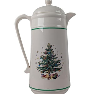 May include: White ceramic coffee carafe with a Christmas tree design. The carafe has a lid, handle, and spout. The Christmas tree is decorated with ornaments and surrounded by presents. Green stripes accent the top and bottom.