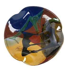 Puede incluir: Un plato de cerámica con un diseño abstracto colorido en tonos de azul, verde, amarillo, rojo y negro. El plato tiene un borde ondulado y está firmado "Ken-F" en la esquina inferior izquierda.