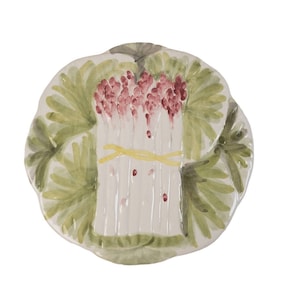 Puede incluir: Un plato de cerámica blanco con un diseño pintado a mano de un manojo de espárragos atado con una cinta amarilla. Los espárragos están rodeados de hojas verdes y bayas rojas.