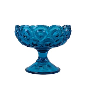 Op de afbeelding: Een turquoise glazen voetkom. De kom heeft een geschulpte rand en een stervormig patroon. De basis is een ronde voet met een bijpassend sterrenpatroon. De kom is gemaakt van transparant glas.