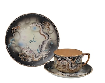 Könnte beinhalten: Ein Vintage-Teetassen- und Untertassen-Set mit einem schwarzen und weißen Drachen-Design. Der Drache ist in Gold, Blau und Rot bemalt. Das Set ist aus Porzellan.