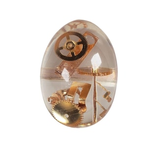 May include: A clear glass egg-shaped ornament filled with gold and copper-colored gears and clockwork parts.