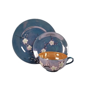 Puede incluir: Un juego de taza y platillo azul y blanco con un diseño floral. El juego incluye una taza de té con un interior marrón claro y un platillo con un diámetro ligeramente más grande.