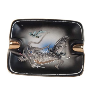 May include: A black ceramic ashtray with a gold rim and a white and blue dragon design.