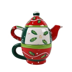 Könnte beinhalten: Ein rotes und grünes Keramik-Teekannen- und Teetassen-Set mit einem Design aus Stechpalme und Beeren. Die Teekanne hat einen Deckel mit einem weißen und roten Design. Die Teetasse hat einen grünen Griff.