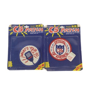 Könnte beinhalten: Zwei Bügelbilder für CB-Funkgeräte. Ein Patch ist rot, weiß und blau mit dem Text "Official CBs of America". Der andere Patch ist blau, weiß und rot mit dem Text "What's Your 20".