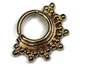 May include: Gold-toned body jewelry with a circular hoop and a decorative design of small beads around the hoop.