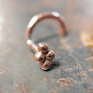 May include: A rose gold nose ring with a cluster of four small round beads.