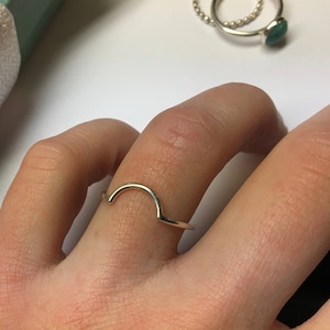 Può includere: Un anello d'argento a forma di arco, indossato su un dito.