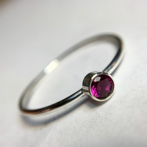 May include: A simple silver band ring with a single, round, dark pink gemstone.