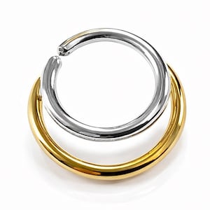 May include: Two hoop earrings, one gold and one silver, are stacked on top of each other. The earrings are circular and have a smooth, polished finish. The background is plain white.