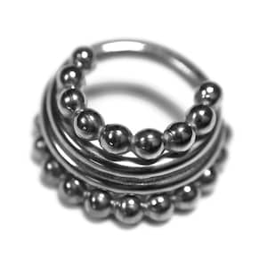 Puede incluir: Un anillo de plata con varias filas de pequeñas cuentas. El anillo está hecho de metal y tiene un acabado liso y pulido.