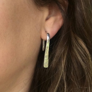 May include: A pair of silver hammered earrings with a curved shape. The earrings are worn in the earlobes.