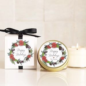 May include: A white square gift box with a black ribbon bow and a round gold-lidded candle, both featuring a festive wreath illustration with red poinsettias, green pine needles, and the text Happy Holidays and The Smiths.