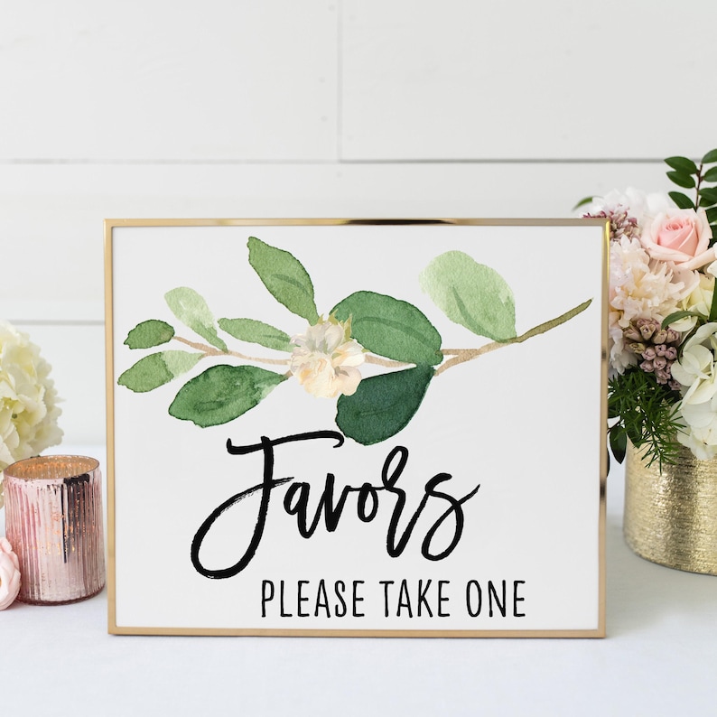 a sign with a floral design and the text "Favorites Please Take One" written on it. The sign is placed on a table, surrounded by flowers and candles.