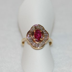 Puede incluir: Un anillo de oro con un rubí ovalado rojo rodeado por un halo de pequeños diamantes.