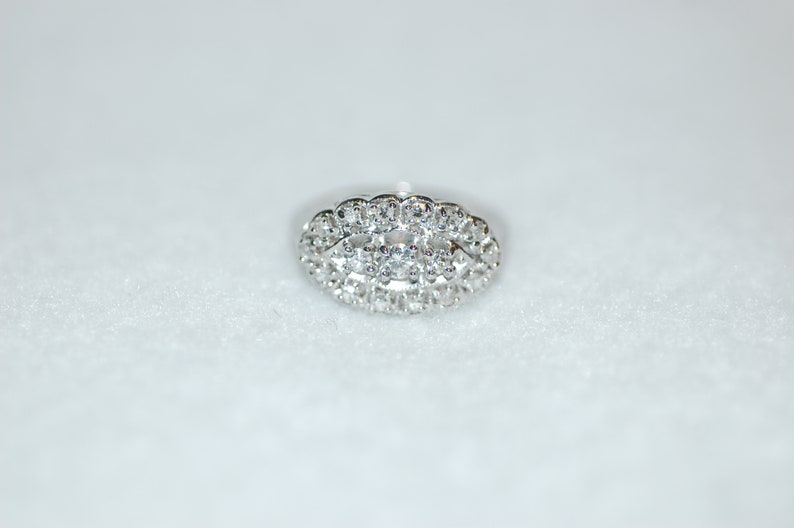 May include: A silver ring with a large oval-shaped cluster of small diamonds.