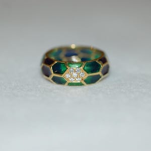 A close-up shot of a gold band ring featuring green and dark enamel in a geometric pattern, centered with a cluster of small diamonds.