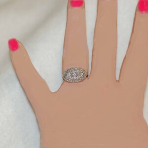 May include: A silver ring with a large oval-shaped center stone surrounded by smaller diamonds.