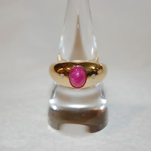 Può includere: Un anello d'oro con una pietra ovale rosa e due diamanti più piccoli sulla fascia.