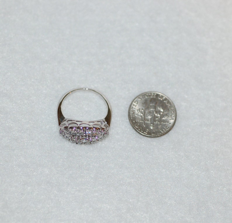 May include: A silver ring with a band of small, clear stones. The ring is shown next to a US dime for size comparison.