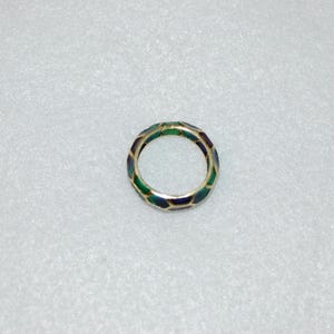 An overhead view of the patterned gold ring showing its continuous hexagonal enamel design in green and dark tones against a plain textured background.
