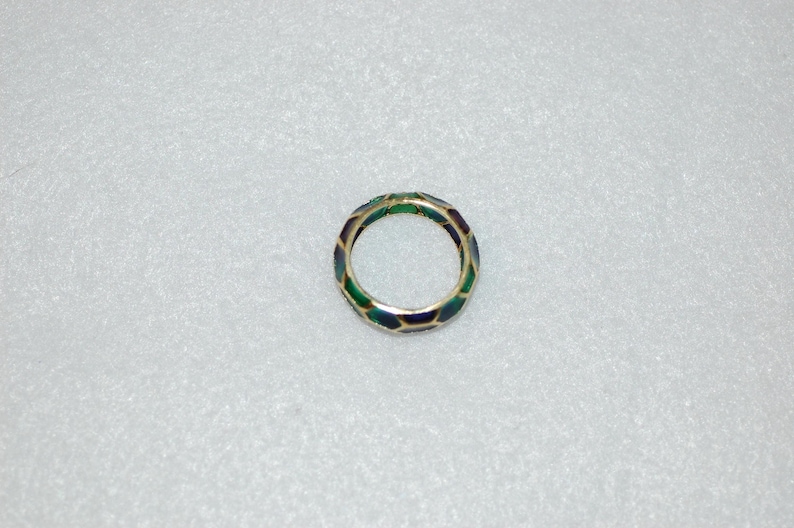 An overhead view of the patterned gold ring showing its continuous hexagonal enamel design in green and dark tones against a plain textured background.