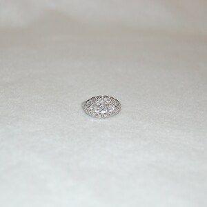 May include: A silver ring with a large oval-shaped cluster of small diamonds.