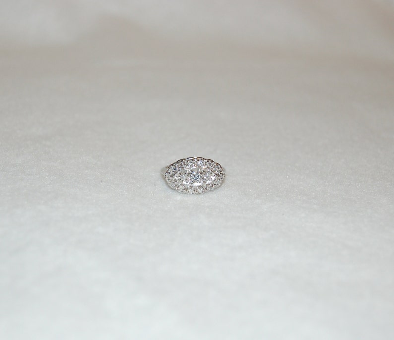 May include: A silver ring with a large oval-shaped cluster of small diamonds.