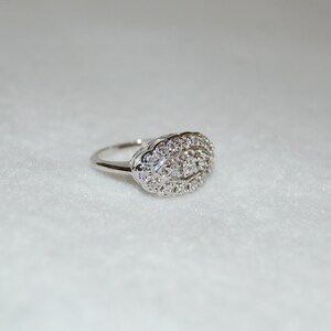 May include: A silver ring with a large oval-shaped cluster of small diamonds.