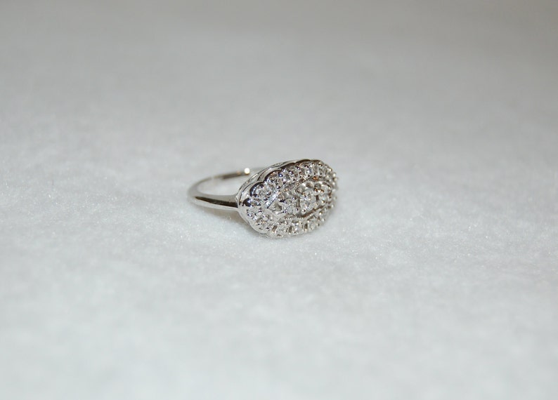 May include: A silver ring with a large oval-shaped cluster of small diamonds.