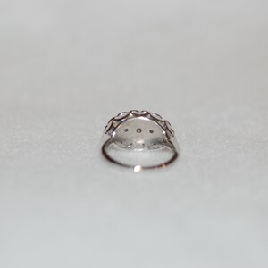 May include: A silver ring with a round, clear stone surrounded by smaller stones. The ring is set in a delicate, intricate design.