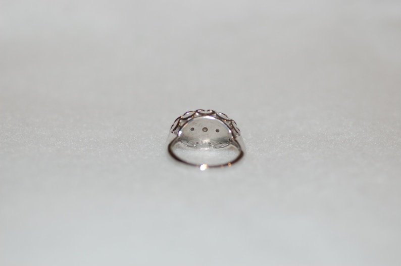 May include: A silver ring with a round, clear stone surrounded by smaller stones. The ring is set in a delicate, intricate design.