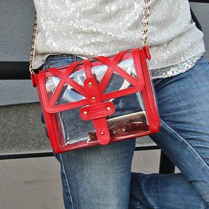 May include: A red and clear plastic crossbody bag with a gold chain strap. The bag has a geometric design and is worn over a denim outfit.
