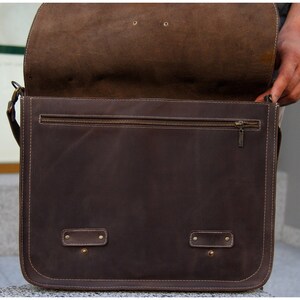 K&ouml;nnte beinhalten: Eine braune Ledertasche mit Rei&szlig;verschlussfach und zwei Schnallen. Die Tasche ist offen und das Innere ist sichtbar.